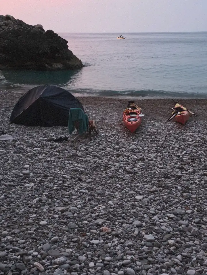 sea kayaks and a camping tent on a remote Adriatic beach during a sea kayaking expedition