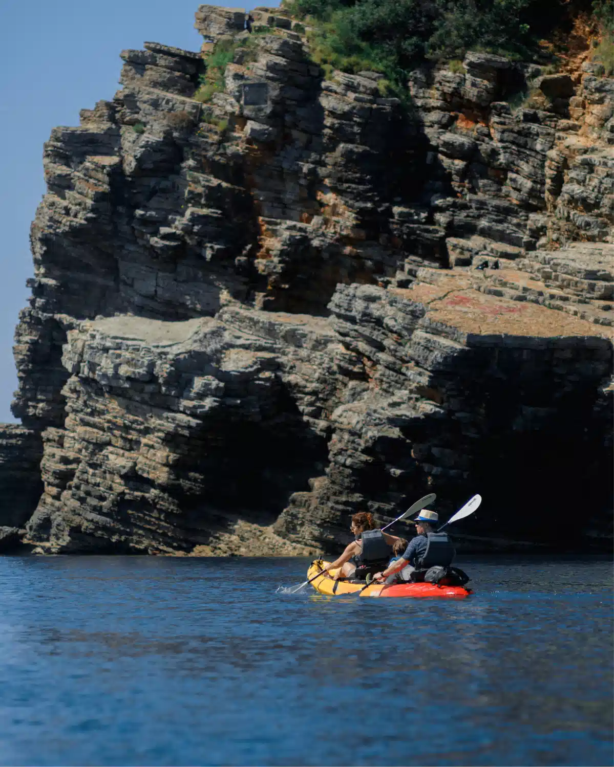 Kayak gliding along a sheer limestone rock face under overhanging cliffs