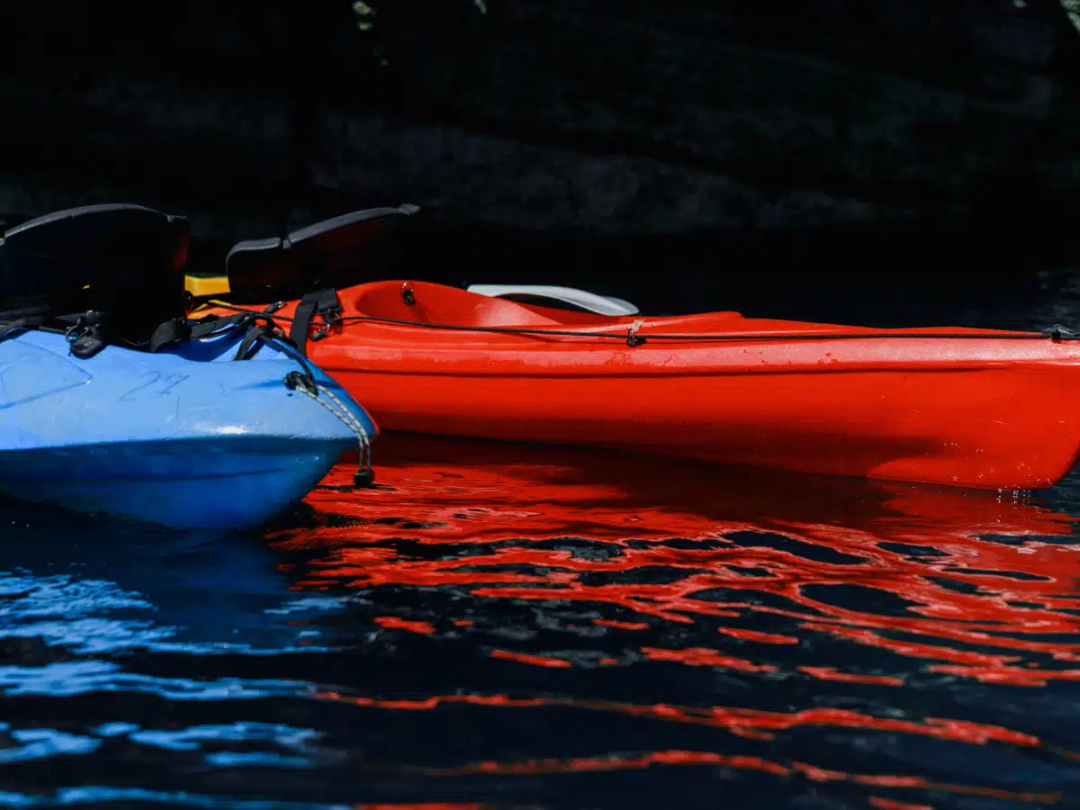 Close-up of red kayak hull and paddle blade floating on crystal-clear turquoise water