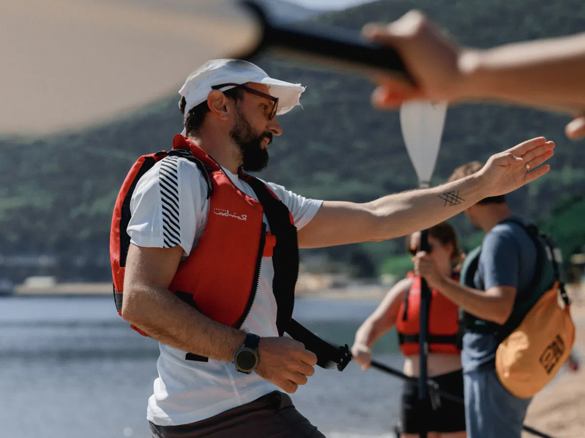 Guide handing a paddle to a guest in a life jacket before entering the coastal cave