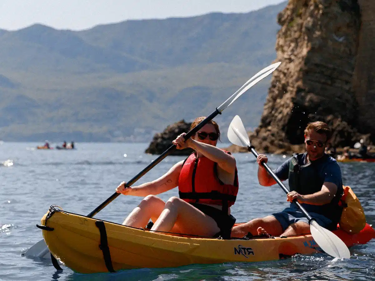 Two kayakers navigating a narrow sea-cave inlet carved into towering limestone walls