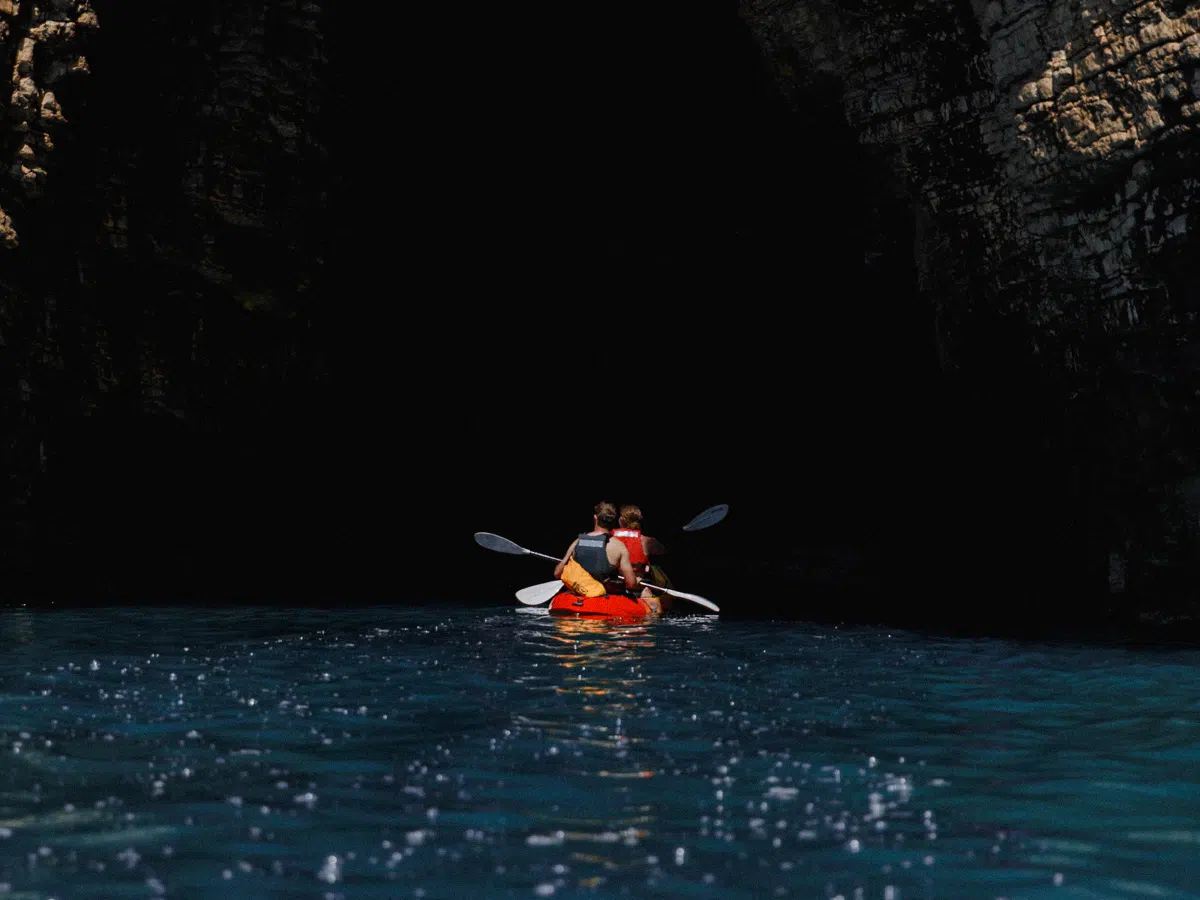Two women paddling a kayak through a narrow cave corridor