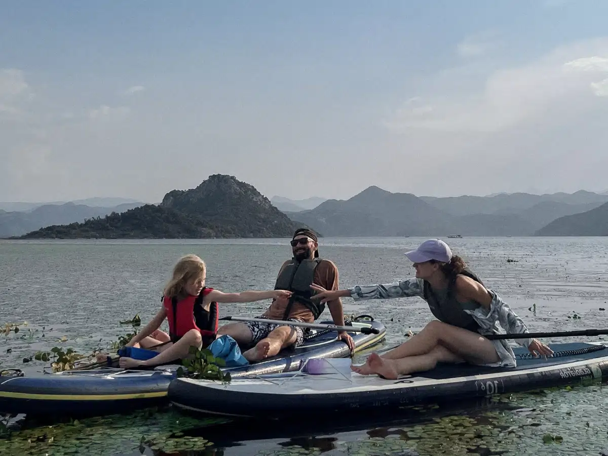 Family relaxing on SUP boards, parent and child reaching hands on Skadar Lake