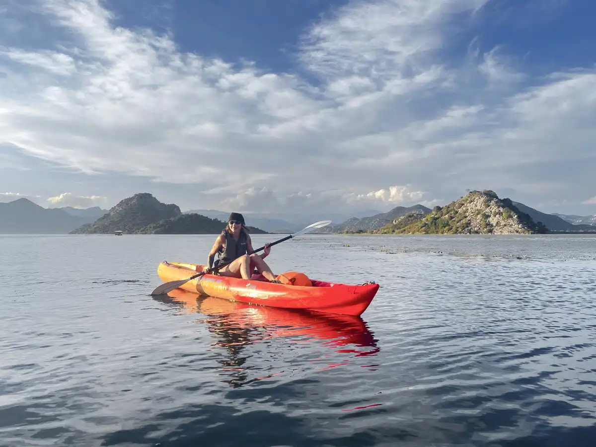 Solo paddler in a red kayak on calm Skadar Lake with small islets and wide sky