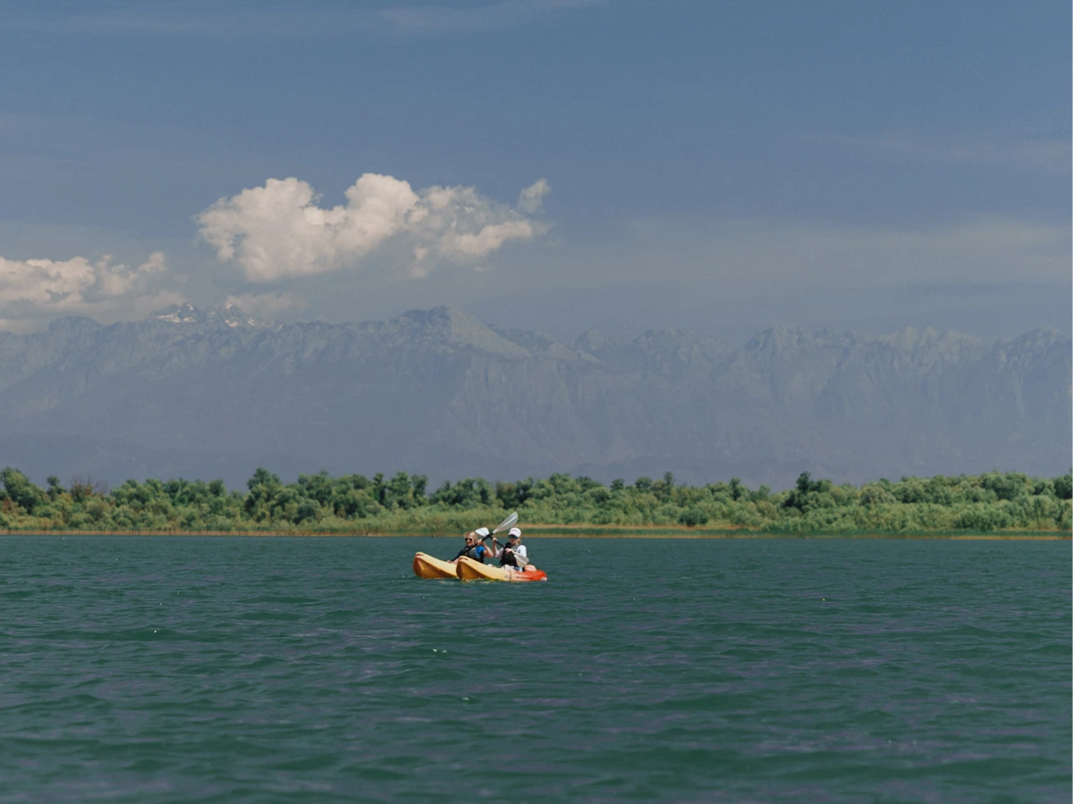 Tandem kayakers crossing open water with a mountain ridge on the horizon