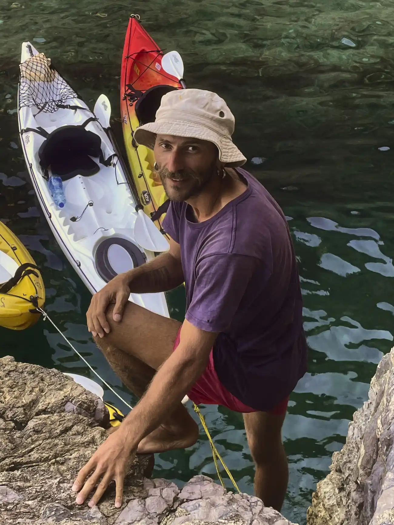 Guide Vasilii standing on rocks by the water next to kayaks