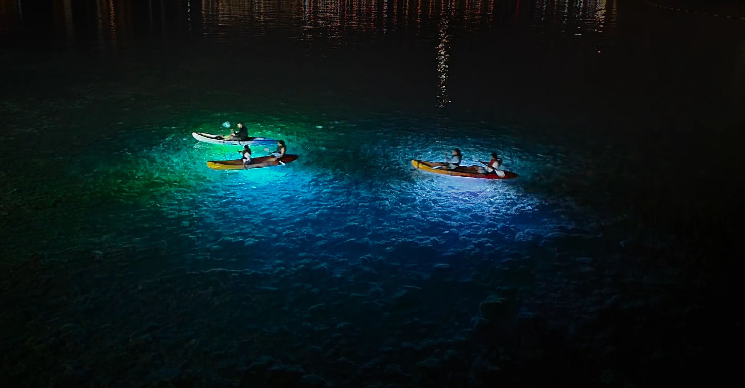 LED-lit kayaks glowing blue on calm night water near Budva old town