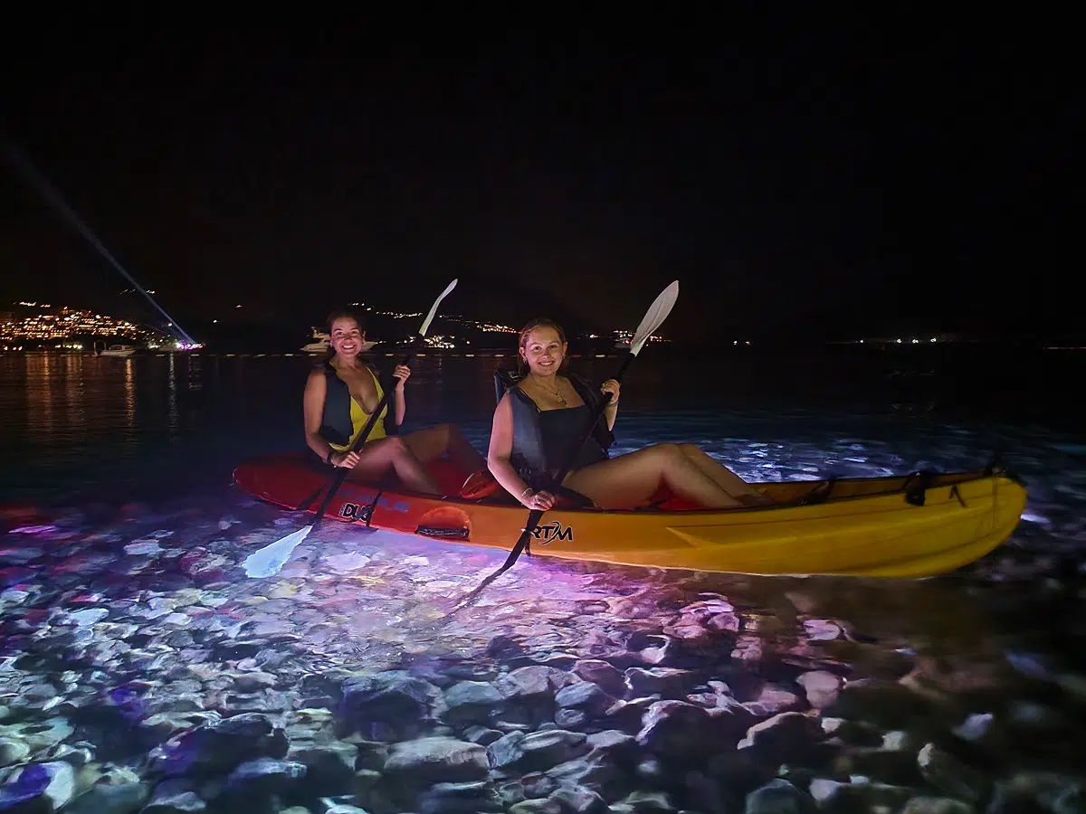 Two women in a tandem kayak above LED-lit water, Night Light tour, Budva