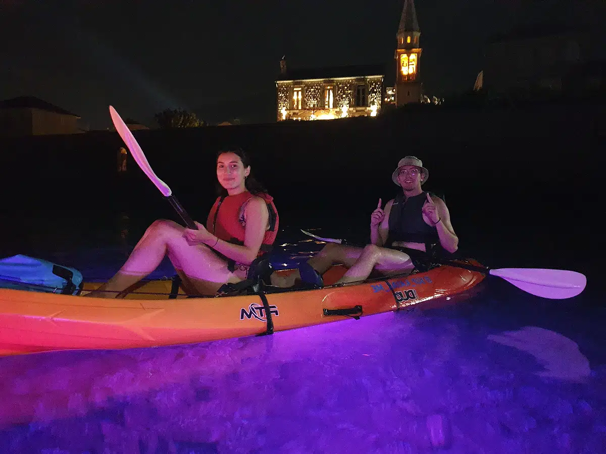 Two paddlers relaxing in an orange kayak under magenta and blue night lights