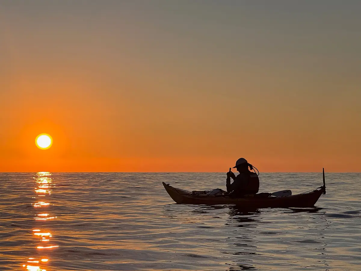 Silhouette of a kayaker on calm sea at sunset