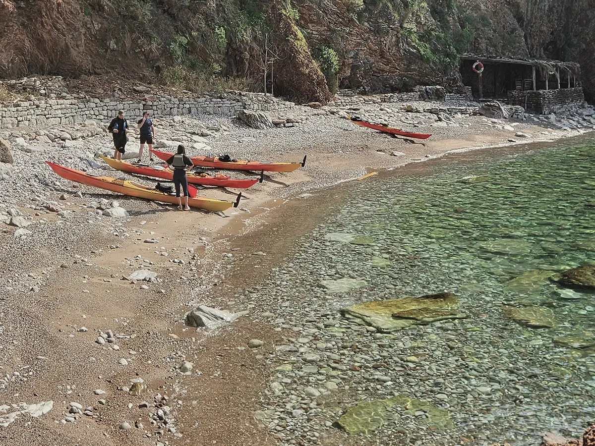 Kayaks pulled up on a quiet pebble beach with clear shallow water