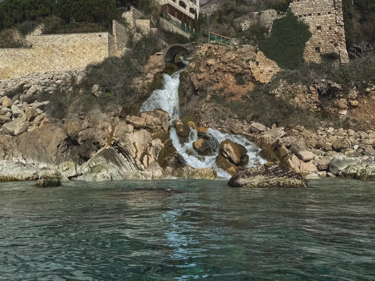 Small coastal waterfall flowing over rocks into the sea below old stone buildings