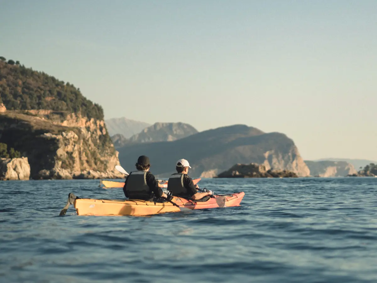 Two people kayaking on open water with a rocky coastline in the distance