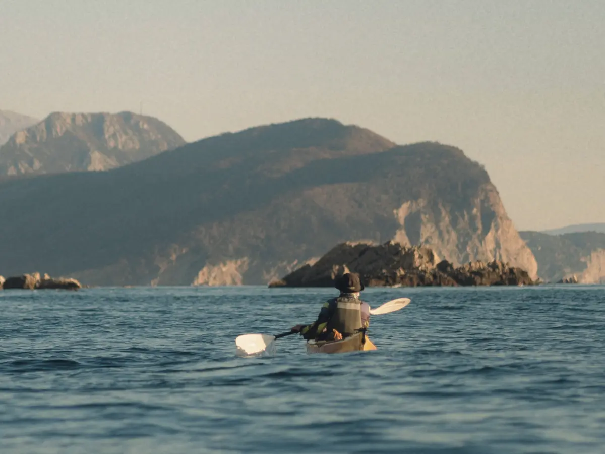 Solo kayaker on calm sea with rocky islands and mountains in the background