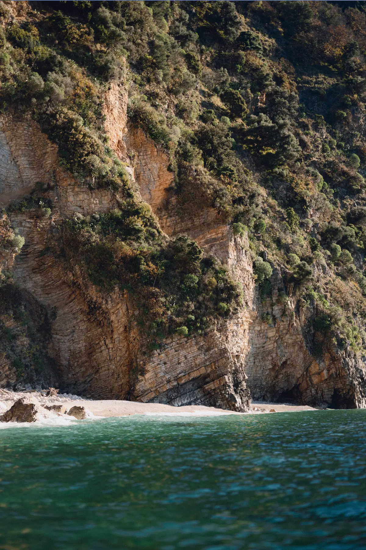 Steep coastal cliff above a small secluded beach and clear sea