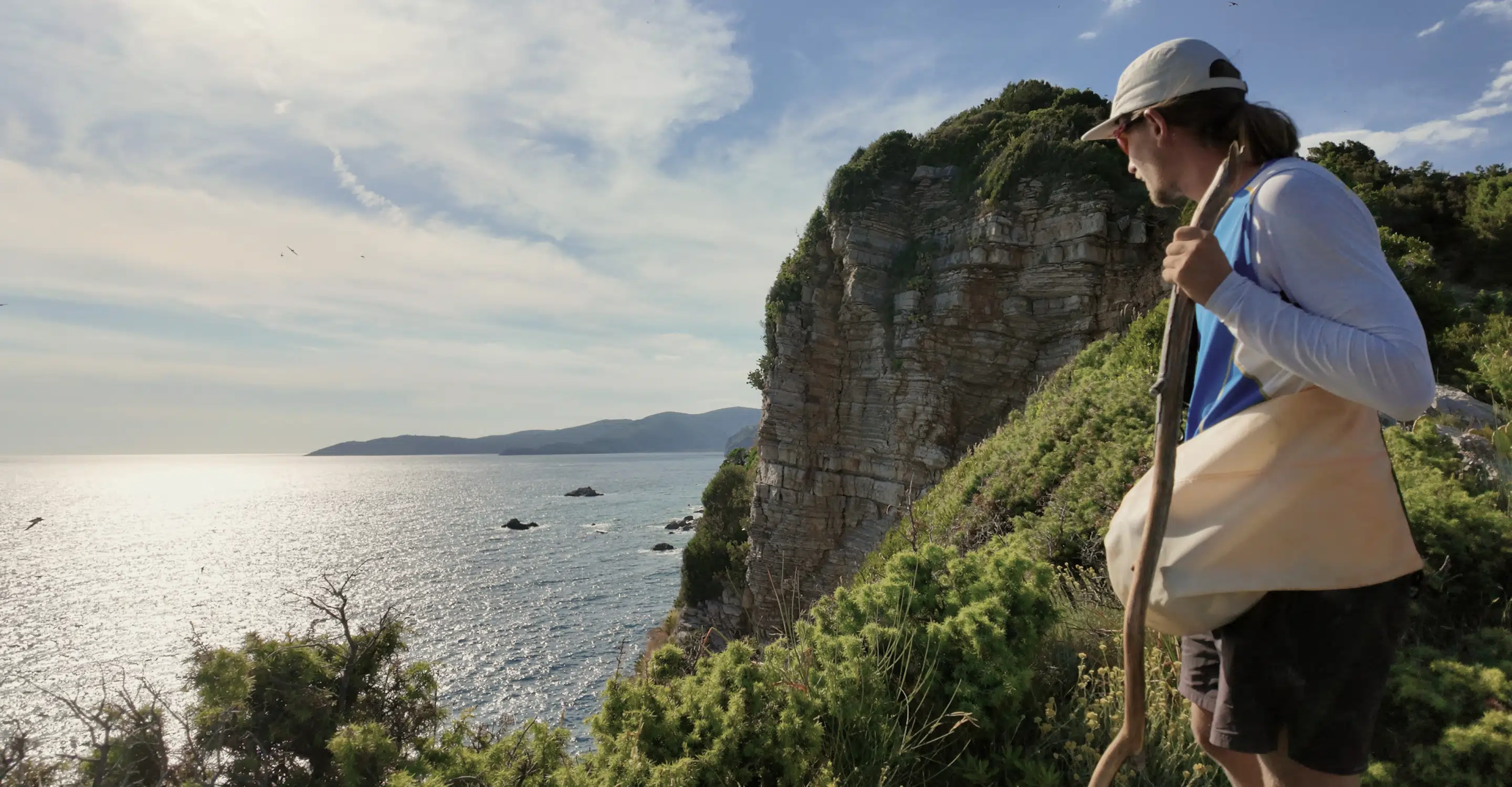 Hiker with daypack walking a coastal trail on Sveti Nikola Island with cliffs and sea views