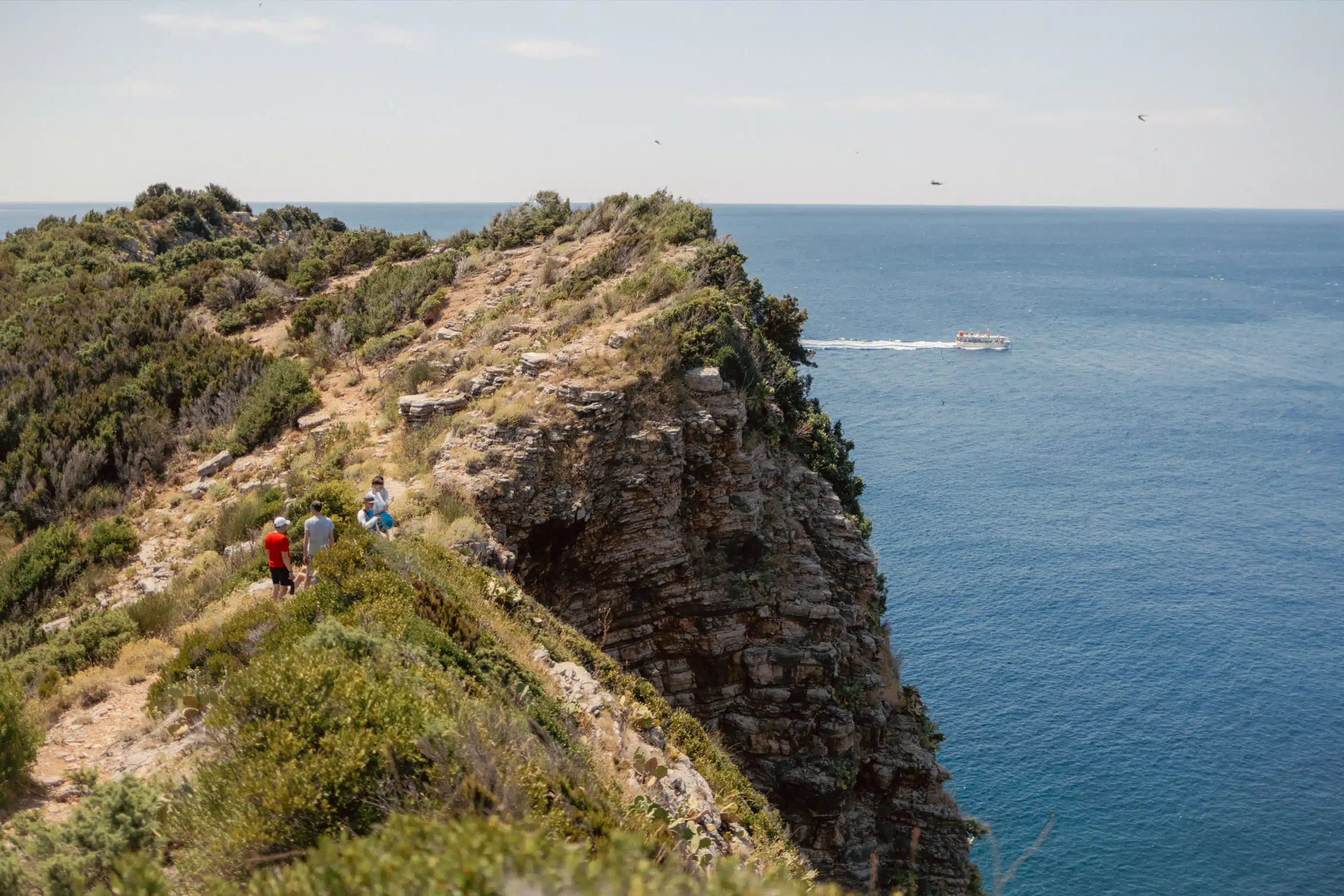 Four hikers walking the high cliff-top ridge above deep blue Adriatic waters