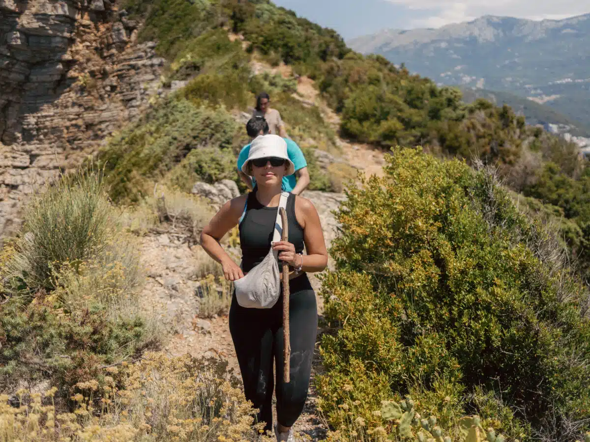 Hikers on a narrow coastal trail; woman in sun hat leading — Sveti Nikola Island