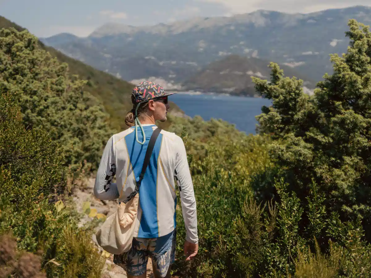 Hiker in a blue shirt standing on a windy ridge with the sea behind