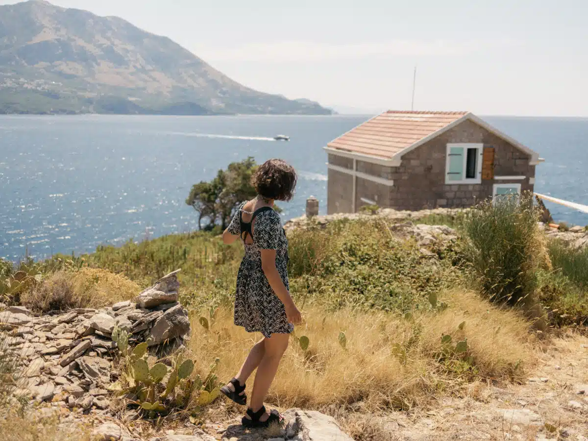 Hiker with backpack passing a small stone lighthouse near the shoreline